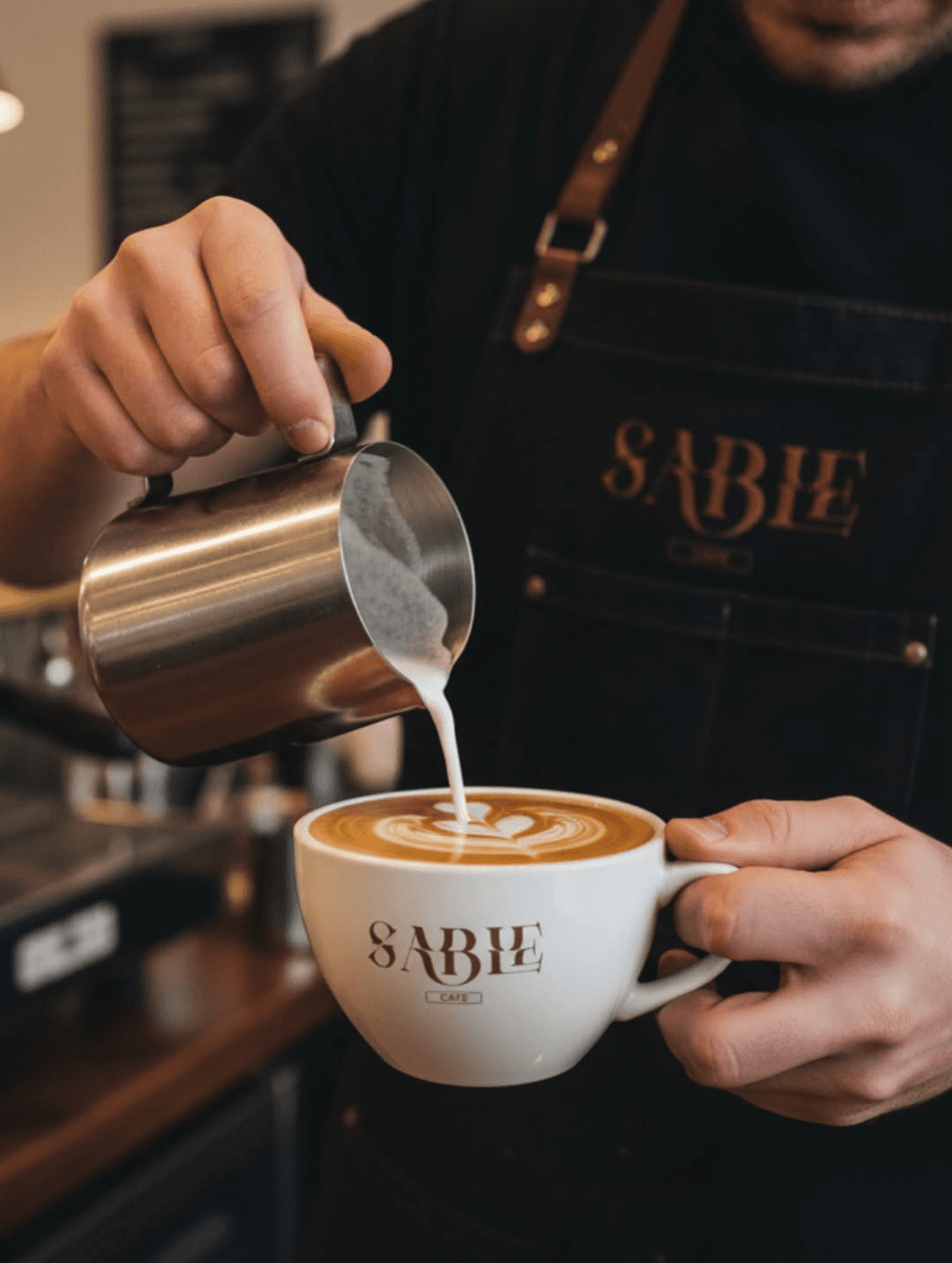 Barista pouring latte art into a branded ceramic cup